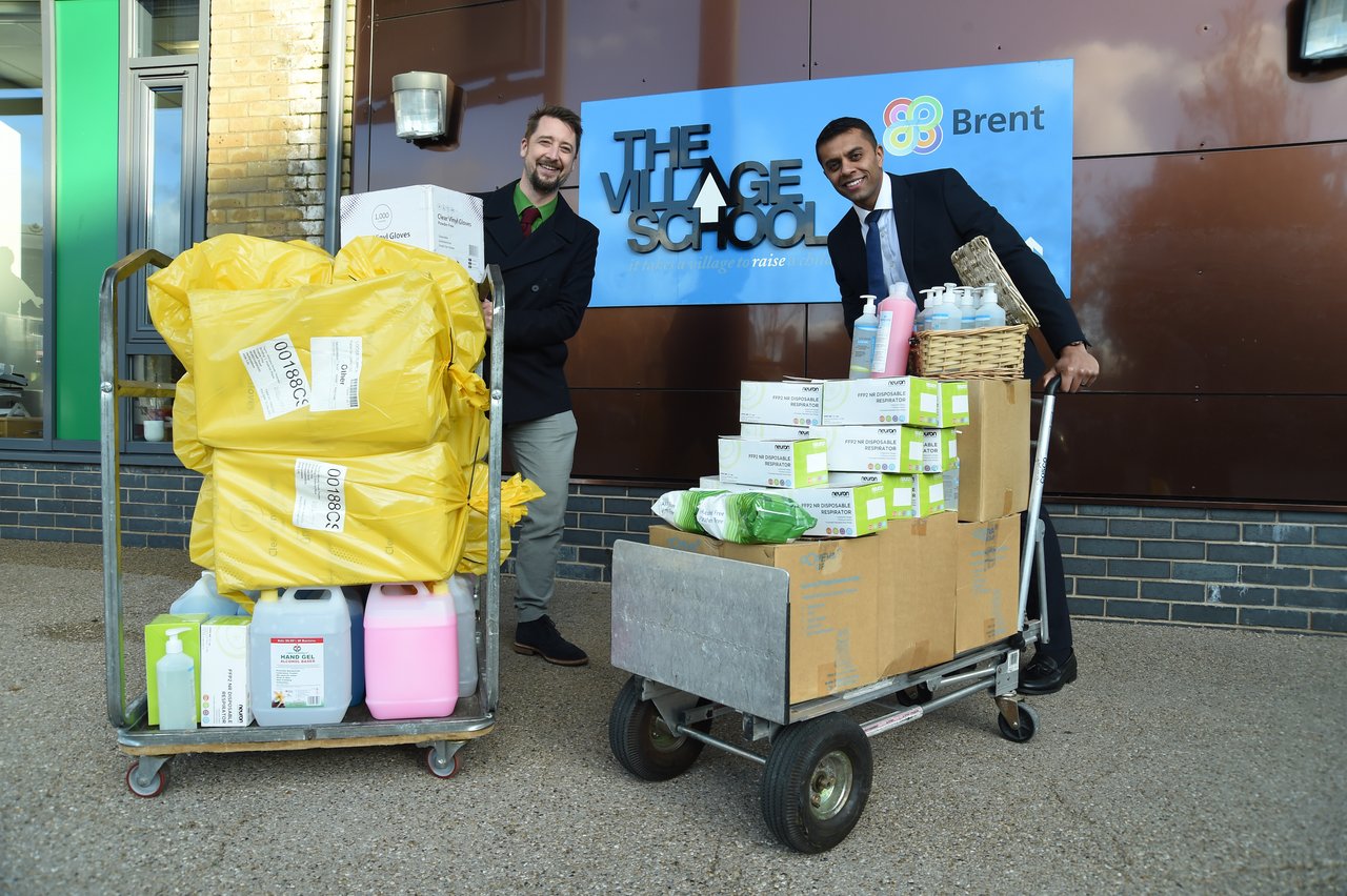 Two people with trolleys full of donations of food and essential items in front of a blue sign that says 'The Village School' in black text.