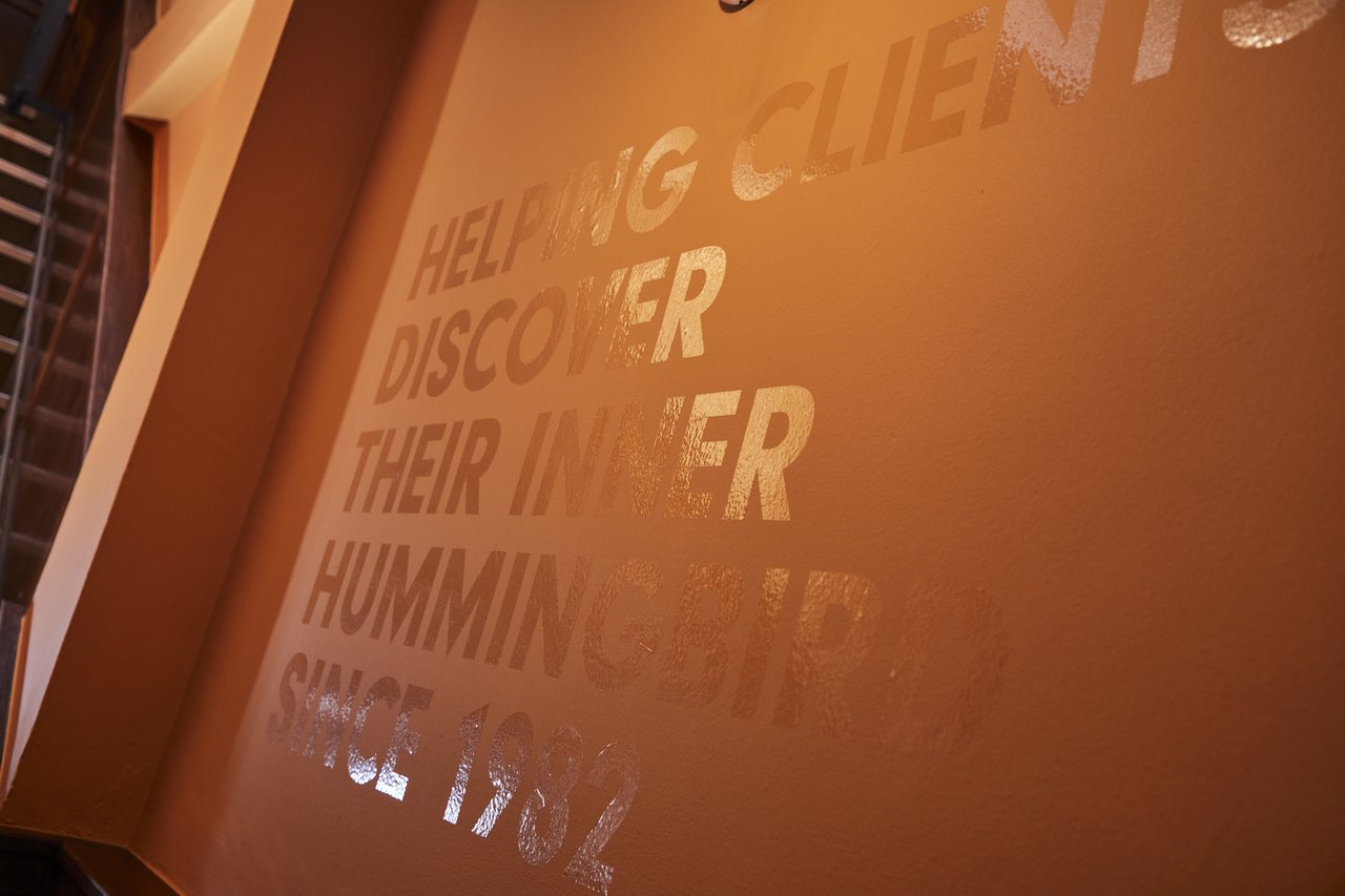 A terracotta wall with a motto on it. The text, in capital letters, reads "Helping clients discover their inner hummingbird since 1982."
