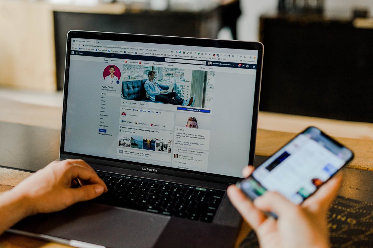 Someone using a laptop and a smartphone, both of which have Facebook on the screen.