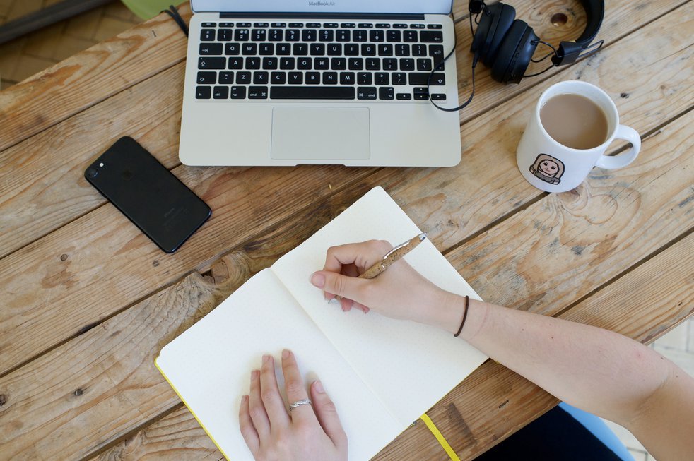 Person writing in a notebook with laptop nearby.