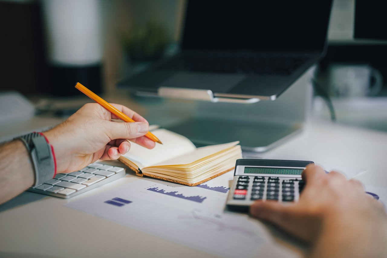 A person using a calculator and writing notes in a notepad