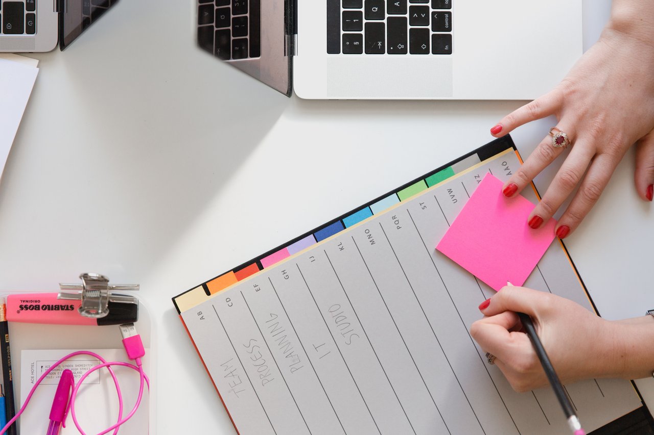 An overhead image of someone writing on a pink Post-It note.