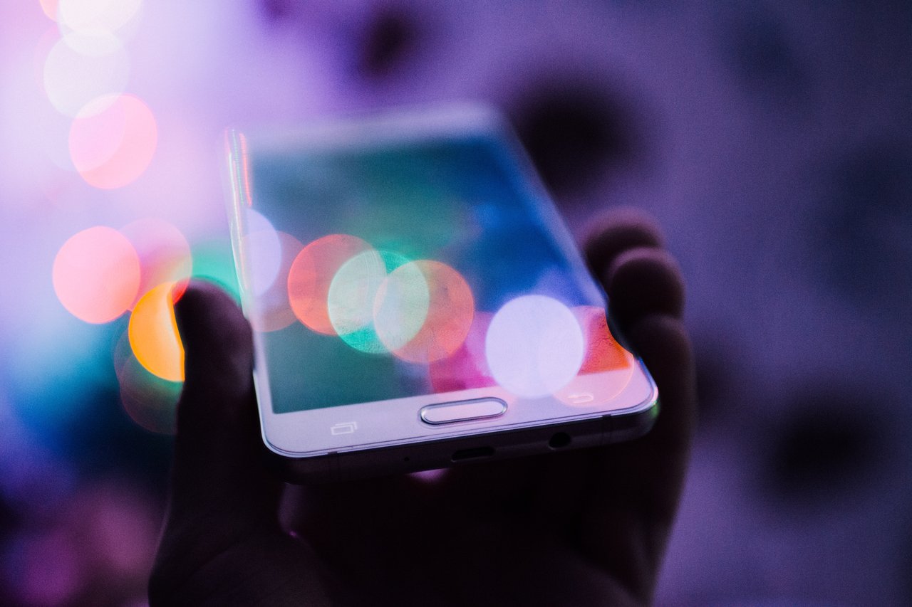 A white smartphone in a persons hand with lens flare on the image.