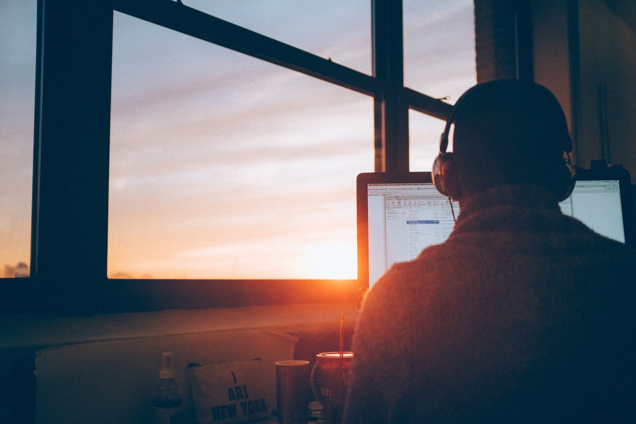 A person working at a computer in front of a window at sunset.