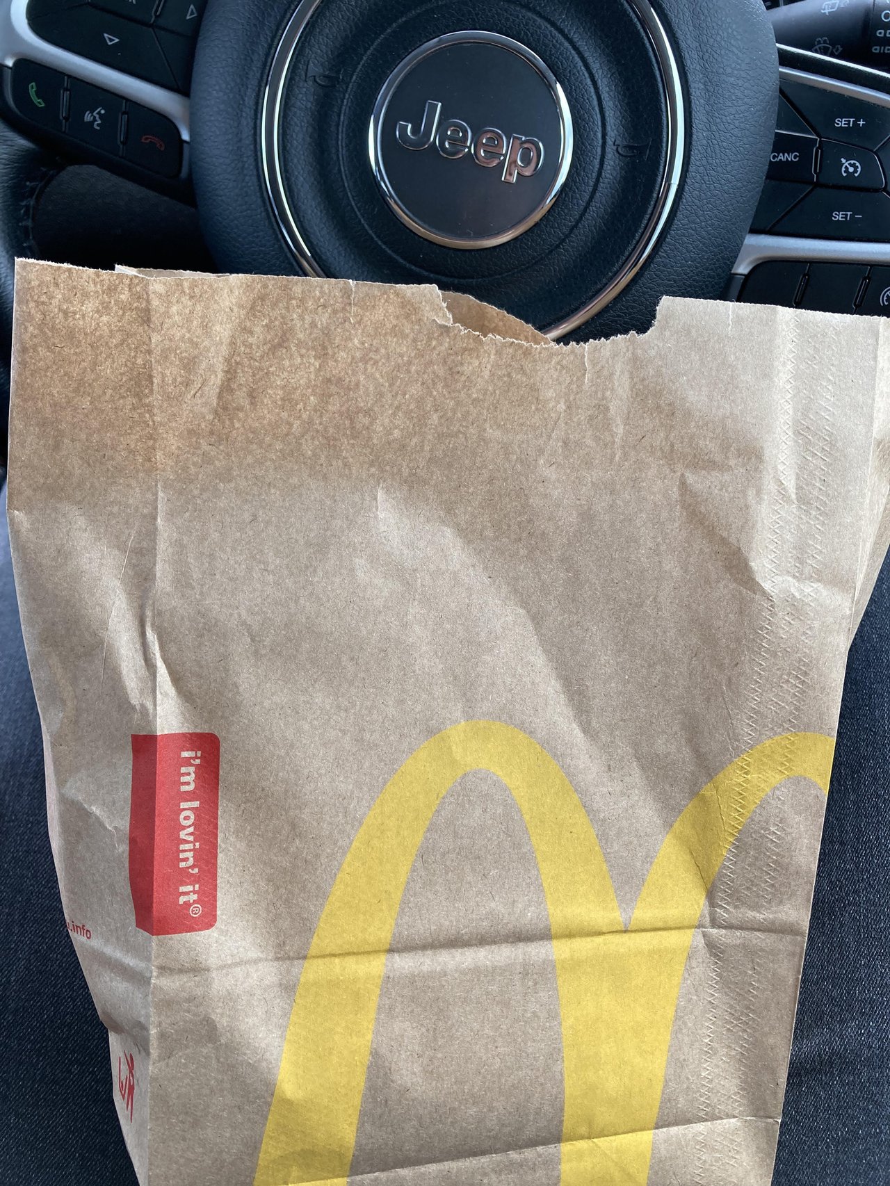 McDonald's bag in front of a car steering wheel